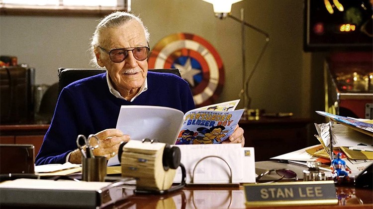 Stan Lee, cartoonist, sitting at his work desk reading a comic book.